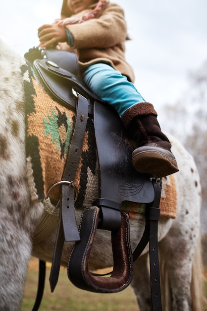 Vertikale Aufnahme eines nicht erkennbaren kleinen Kindes, das auf einem winzigen Appaloosa-Pony sitzt