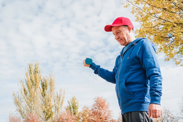 Vertikale Aufnahme eines sportlichen Mannes mittleren Alters in Sportbekleidung, die mit Hanteln in einem Park arbeitet