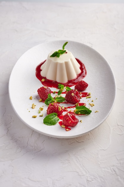 Vertikale Ausrichtung Panna Cotta mit Himbeersirup, Pistazien, Beeren und Minze oin ovale Platte