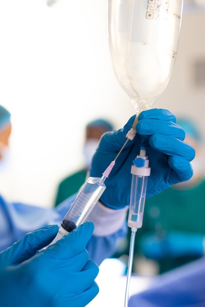 Vertikale Darstellung der behandschuhten Hand eines Chirurgen, der den Infusionsbeutel im Operationssaal vorbereitet, mit Kopierraum. Krankenhaus-, medizinische und Gesundheitsdienstleistungen.