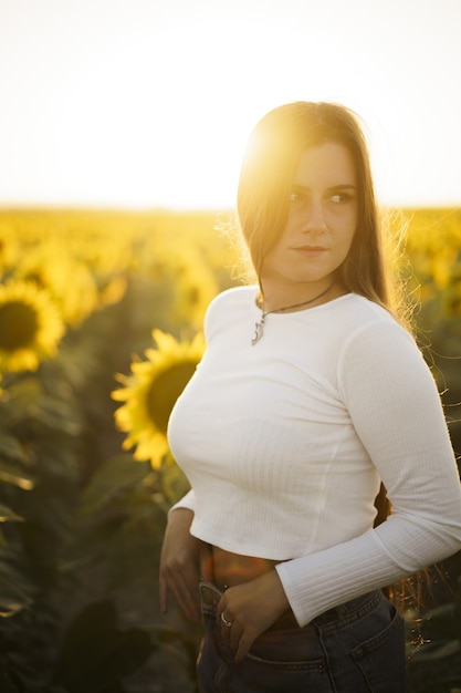 Vertikale flache Fokusaufnahme einer hübschen europäischen Frau in einem Sonnenblumenfeld bei Sonnenaufgang