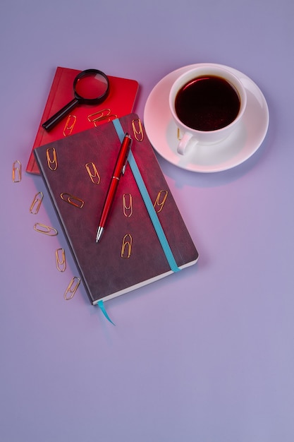 Vertikale geschossene Draufsichtkaffeetasse mit Stift und Schreibheft. Auf lila Hintergrund isoliert.