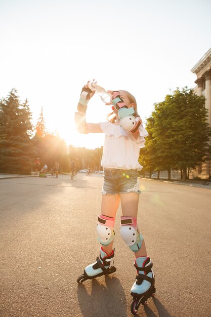 Foto vertikale low angle shot eines mädchens in schutzausrüstung und rollerblades, trinkwasser an heißen sommertagen