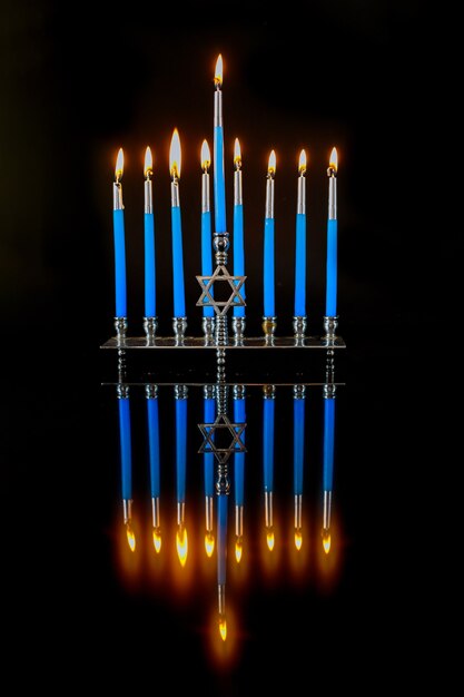 Vertikale Menora mit blauen brennenden Kerzen und Reflexion auf Oberfläche für Chanukka jüdischen Feiertag.