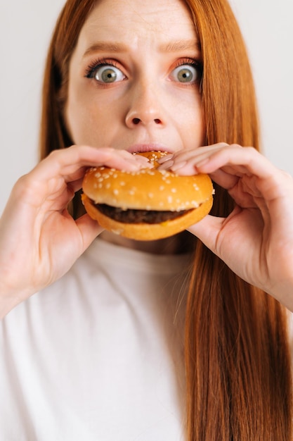 Vertikale Nahaufnahme einer überraschten süßen jungen Frau mit weit geöffneten Augen, angenehmer Biss, appetitanregend