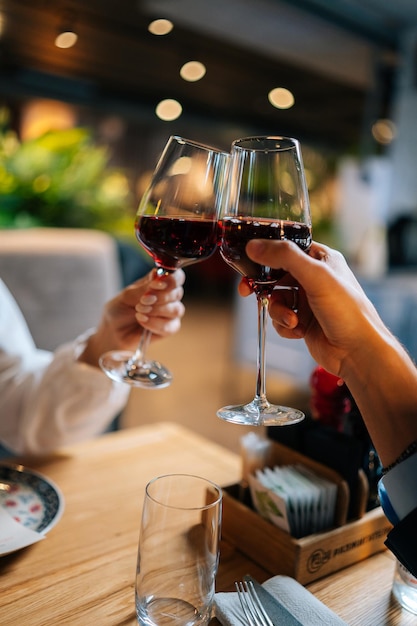 Vertikale Nahaufnahme eines liebenden Mannes und einer Frau, die abends im Restaurant am Tisch mit Rotwein klirren