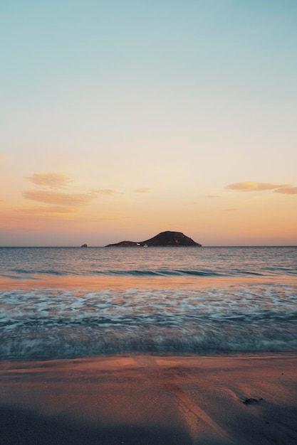 Vertikale Ozean Sunrise Landschaft mit Insel und bunten Himmel im Hintergrund Wellen und Küsten auf Meerwasser im Morgenlicht Leerer Himmel copyspace Schönheit der Natur Meereslandschaft im Sonnenuntergang stimmungsvollen Abenddämmerung