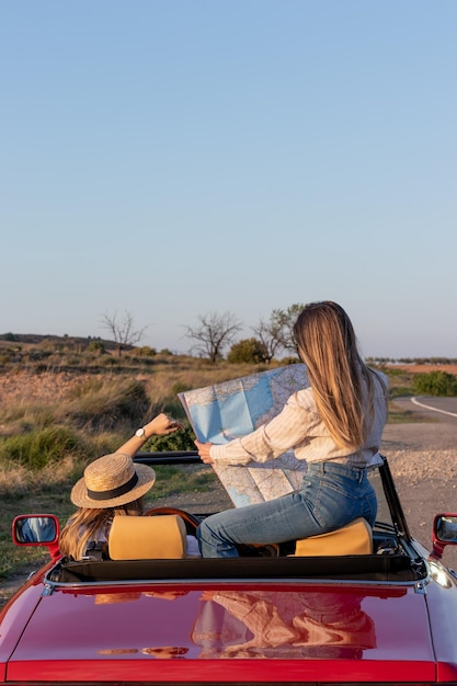 Vertikale Rückansicht von nicht erkennbaren Frauen, die in einem roten Retro-Cabrio mit Kopierraum sitzen und eine Karte lesen