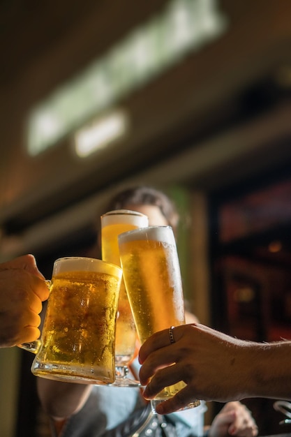 Vertikaler Schuss männlicher Hände, die mit Gläsern erfrischendem kaltem Bier in der Bar klirren