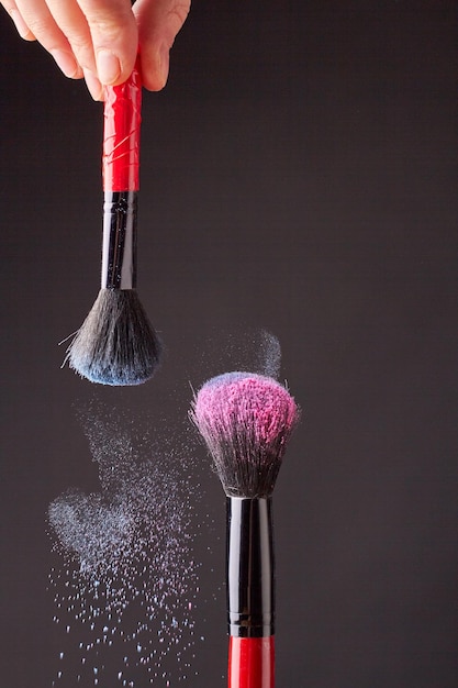 Vertikaler Schuss zwei Make-upbürsten der Frauen mit farbigem Puder
