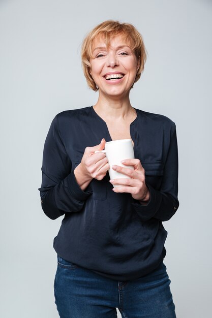 Vertikales Bild der lachenden älteren Frau, die Tasse Tee hält