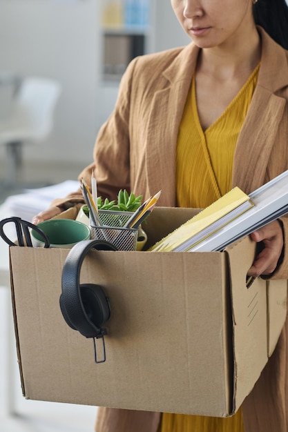 Vertikales Bild einer Geschäftsfrau, die ihre Sachen nach dem Jobverlust in eine Schachtel packt