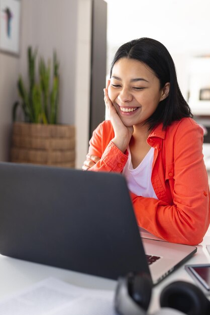 Vertikales Bild einer glücklichen biracial Frau, die zu Hause lächelnd einen Videoanruf auf einem Laptop führt, Platz zum Kopieren. Arbeiten von zu Hause aus, Technologie, Kommunikation und Lifestyle-Konzept.