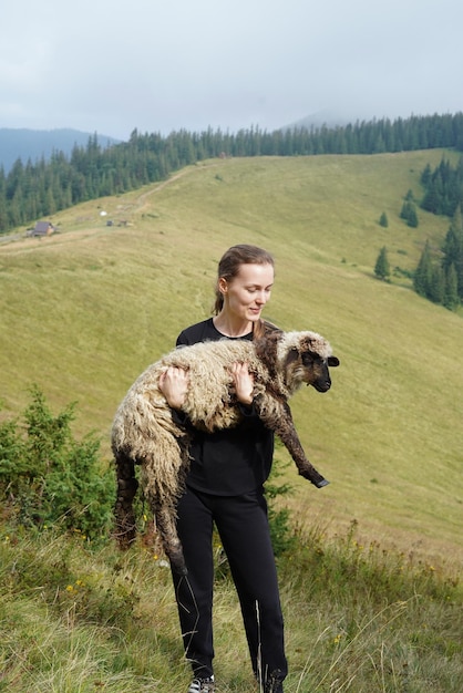 Vertikales Bild einer jungen Schäferin, die ein Schaf in den Bergen hält Small Business Farming und Liebe zum Naturkonzept