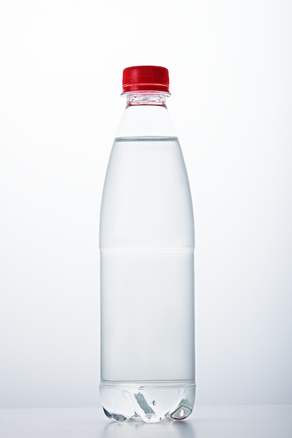 Vertikales Bild einer Plastikflasche mit rotem Deckel gefüllt mit Wasser auf weißem Hintergrund