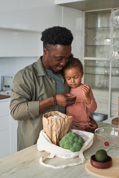 Vertikales Bild eines afroamerikanischen Vaters mit seiner kleinen Tochter, die in der Küche steht