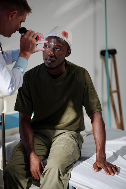 Vertikales Bild eines professionellen Arztes, der verwundete Soldaten im Krankenhaus untersucht