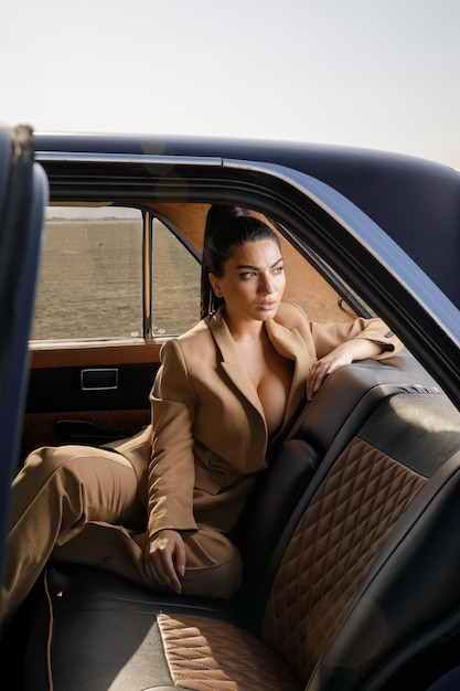 Vertikales Foto der jungen Dame auf dem Rücksitz des Autos Sexy junges Modell, das zur Seite schaut Hochwertiges Foto