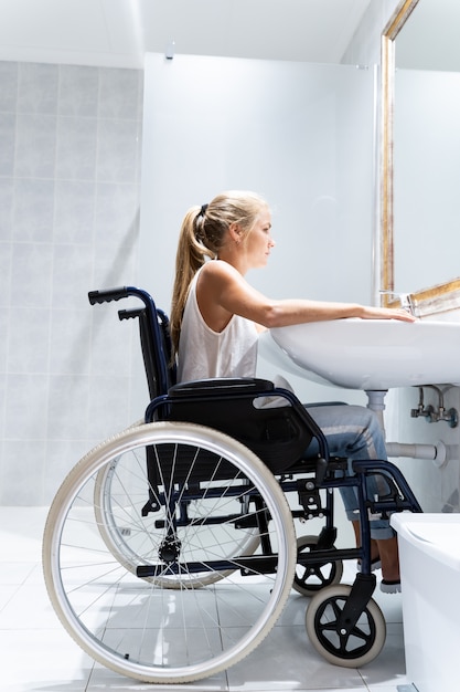 Vertikales Foto einer blonden Frau, die in einem Rollstuhl in einem Badezimmer sitzt