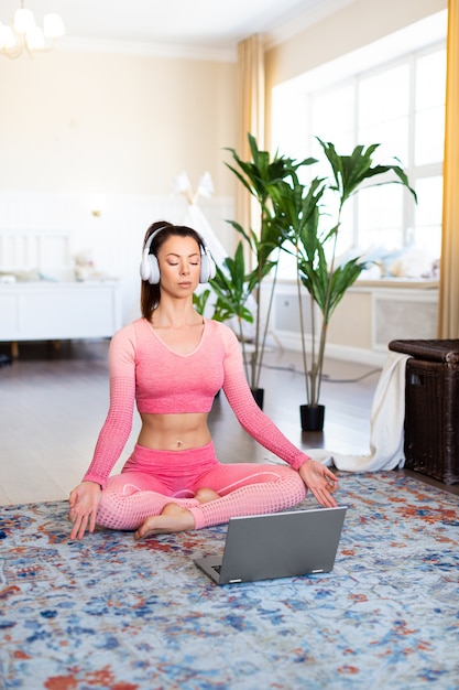 Vertikales Foto einer Frau meditiert zu Hause vor einem Laptop-Monitor Online-Yoga-Lektion während der Quarantäne