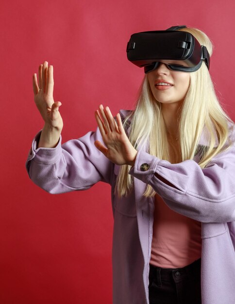 Vertikales Foto einer jungen Blondine, die ihre Hände in der Luft offen hält und eine VR-Brille trägt