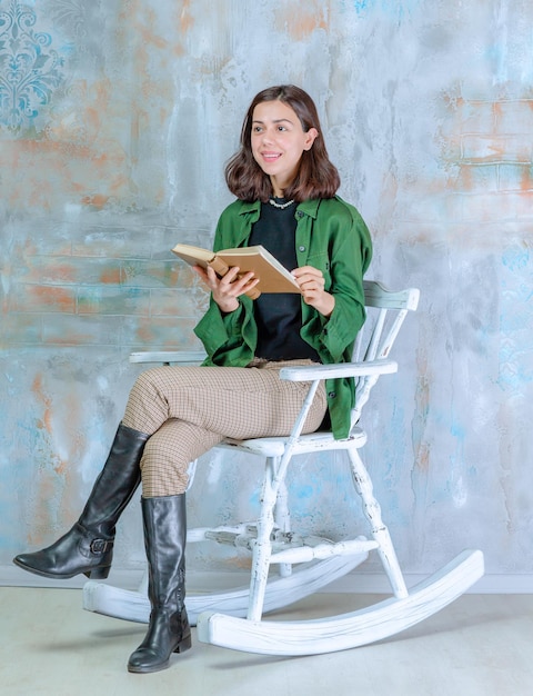 Vertikales Foto einer jungen Dame, die auf dem Schaukelstuhl sitzt und ein Buch hält Foto in hoher Qualität