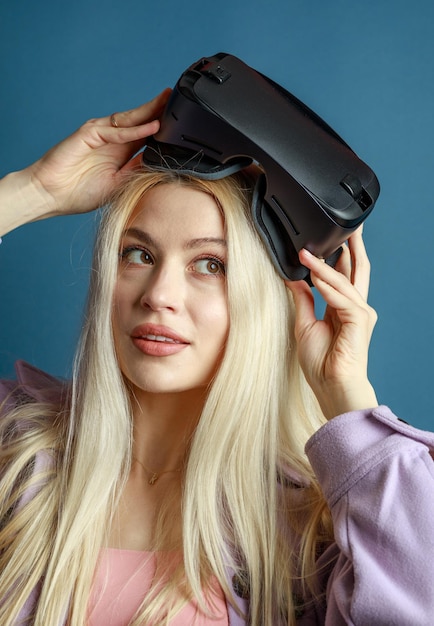 Vertikales Foto einer jungen Dame, die versucht, eine VR-Brille auf blauem Hintergrund zu tragen