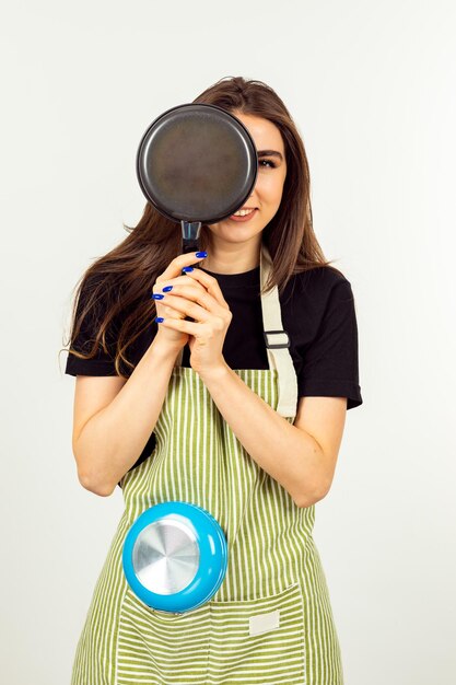 Vertikales Foto eines jungen Mädchens, das auf weißem Hintergrund eine Bratpfanne an ihr Gesicht hält