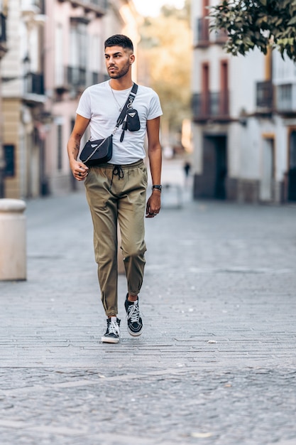 Vertikales Foto eines jungen Mannes, der abgelenkt durch die Straße geht, gekleidet in Freizeitkleidung