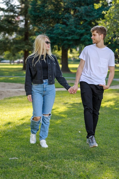 Vertikales Foto eines jungen Paares, das sich an den Händen hält und im Park spazieren geht