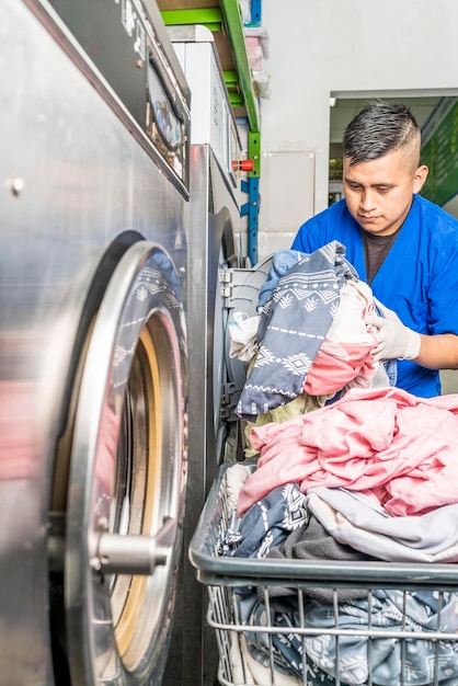 Vertikales Foto eines Mitarbeiters, der Kleidung in eine Industriewaschmaschine einlegt