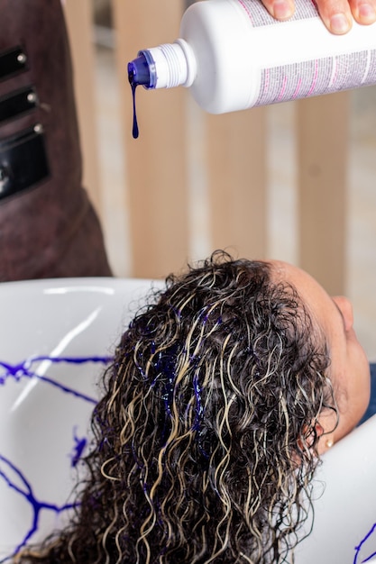 Vertikales Foto eines professionellen Stylisten, der lila Shampoo auf das Haar einer Frau aufträgt