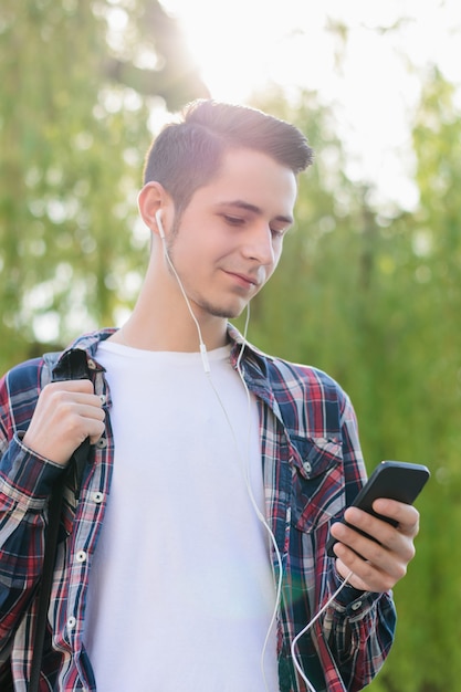 Vertikales Fotoporträt eines gutaussehenden, fröhlichen, ruhigen, neugierigen Kerls in kariertem Outfit und weißem T-Shirt mit mobilem MP3-Player