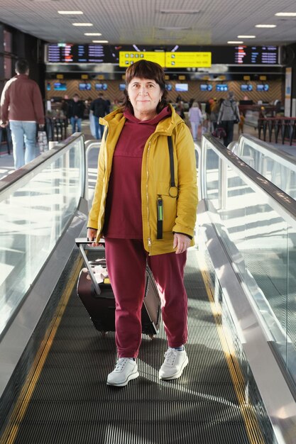 Vertikales Ganzkörperporträt einer älteren Frau mit einem Koffer am Flughafen