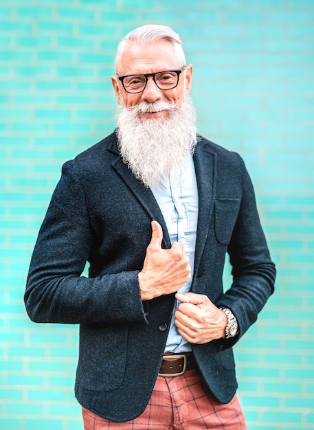 Vertikales Porträt des Hipster-Mannes mit elegantem Outfit, das gegen türkisfarbenen Wandhintergrund aufwirft