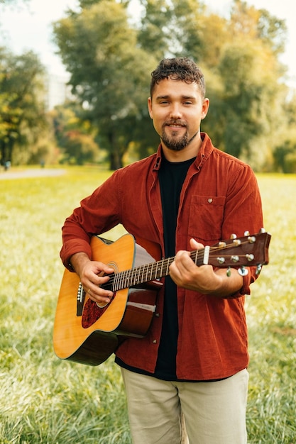 Vertikales Porträt eines jungen gutaussehenden Mannes, der Akustikgitarre in einem Park spielt