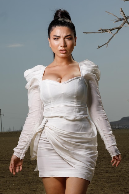 Vertikales Porträt eines jungen, heißen Mädchens in weißem Kleid und mit Blick auf die Kamera Foto in hoher Qualität