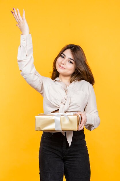 Vertikales Porträt eines jungen Mädchens, das eine Geschenkbox hält und die Hand in der Luft hält Foto in hoher Qualität
