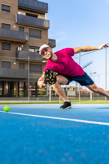 Vertikales Porträt eines jungen Pickleballspielers, der ein Outdoor-Spiel spielt Spieler in Bewegung, der sich ausstreckt, um den Ball zu schlagen