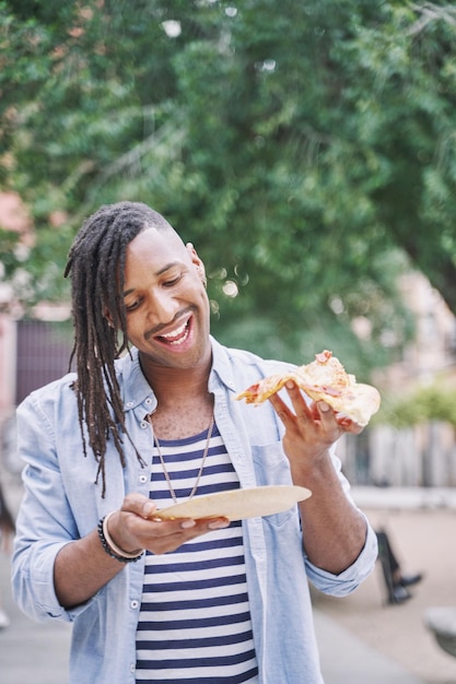 Vertikales Porträt eines Mannes, der ein Stück Pizza in der Hand hält, Fast-Food- und Lifestyle-Konzept