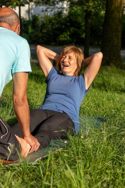 Vertikales Porträt von Mann und Frau, die sich bemühen, Situps zu machen und einen gesunden Lebensstil im Gras und in der Natur zu haben