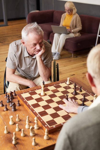 Vertikales Porträt von zwei älteren Männern, die Schach spielen und Aktivitäten im gemütlichen Pflegeheim genießen