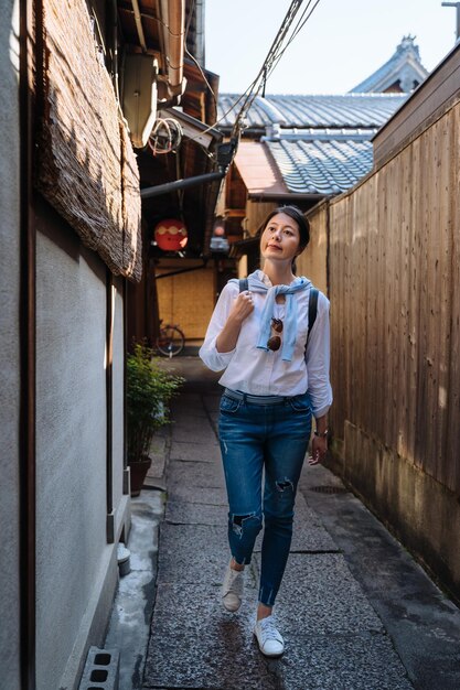 Vertikales sorgloses asiatisches Mädchen in voller Länge, das eine schmale Gasse zwischen traditionellen japanischen Gebäuden in der Hanamikoji-Straße in Gion, Japan, erkundet und durchgeht.