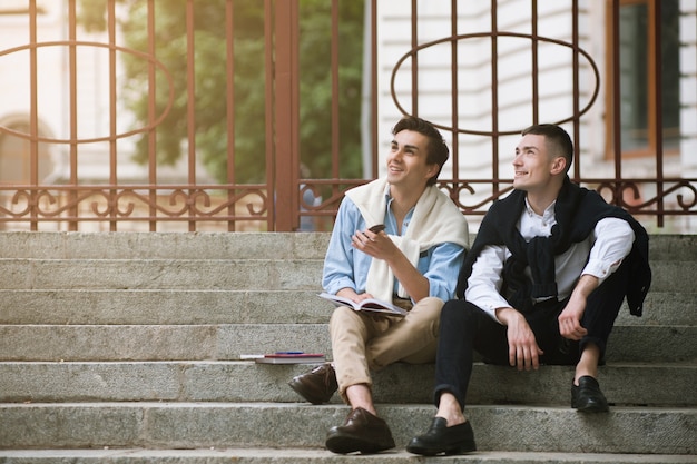 Verträumte Studenten in der Pause draußen. Hintergrund mit zwei glücklichen Männern, Straßenhippieart, junge Männer draußen