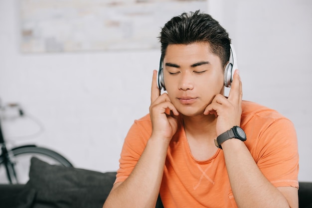 Verträumter asiatischer Mann, der mit geschlossenen Augen Musik über Kopfhörer hört