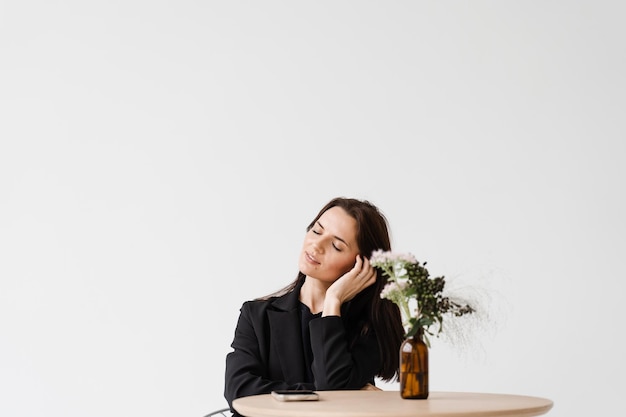 Verträumtes, fröhliches Mädchen, das im Business-Stil gekleidet ist, sitzt am Tisch im weißen Café Porträt einer attraktiven jungen Frau auf weißem Hintergrund