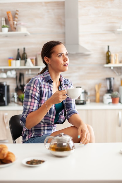 Verträumtes Mädchen, das beim Frühstück in der Küche heißen grünen Tee genießt