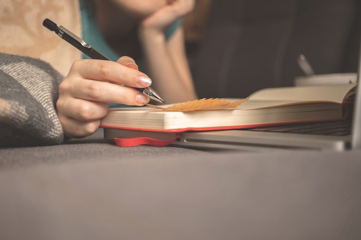 Foto verträumtes mädchen schreibt in den herbstferien ein tagebuch zu hause, das auf einem sofa mit warmem plaid sitzt. hand mit bleistift und herbstlaub auf buch