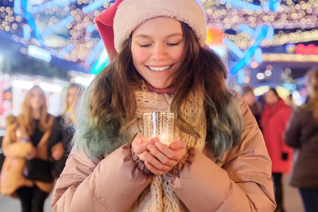 Verträumtes schönes jugendlich Mädchen im Weihnachtsmannhut mit brennender Kerze