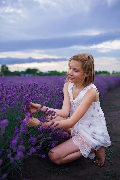 Verträumtes Teenager-Mädchen geht zwischen lila Blumen in den Sommerferien bei schönem Sonnenuntergang spazieren